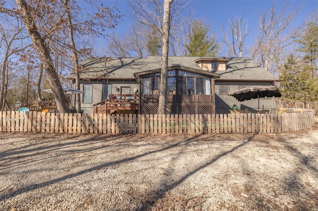 exterior space with a fenced front yard, roof with shingles, a wooden deck, and a sunroom