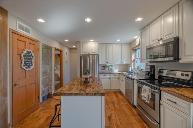 kitchen with visible vents, a kitchen island, a sink, stainless steel appliances, and light wood-style floors