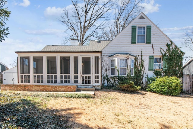 back of property with roof with shingles, a sunroom, and a chimney