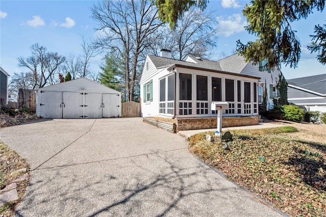 view of side of property featuring a shingled roof, fence, a chimney, a sunroom, and an outbuilding