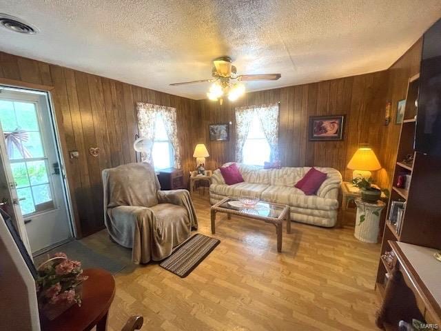 living area featuring visible vents, a textured ceiling, wood finished floors, wood walls, and ceiling fan