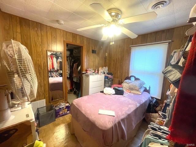 bedroom with a spacious closet, visible vents, wood walls, wood finished floors, and a closet