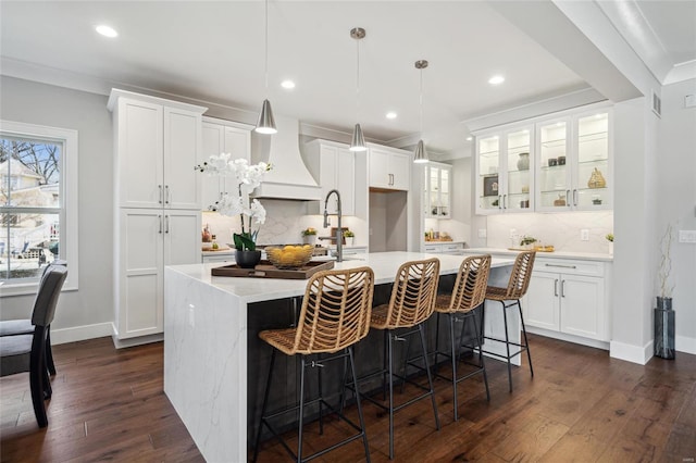 kitchen with a center island with sink, white cabinetry, light countertops, glass insert cabinets, and dark wood-style flooring