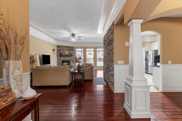 living area with a fireplace, wainscoting, crown molding, decorative columns, and ceiling fan