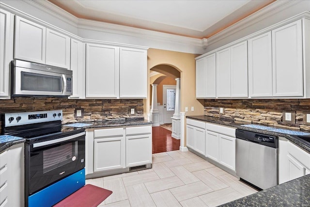 kitchen featuring dark stone countertops, stainless steel appliances, arched walkways, white cabinets, and decorative backsplash