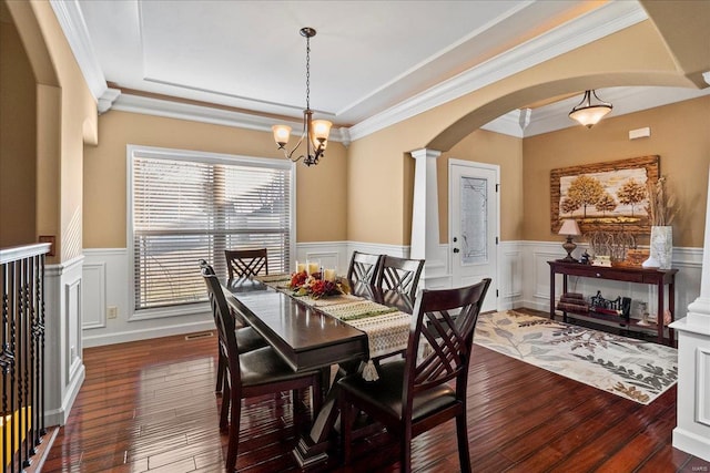 dining space featuring a wainscoted wall, decorative columns, dark wood-style floors, and arched walkways