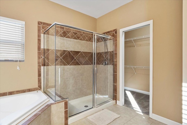 full bathroom featuring a spacious closet, baseboards, a stall shower, a bath, and tile patterned floors