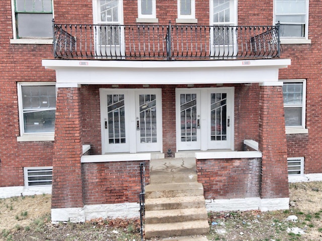 property entrance featuring a balcony, french doors, and brick siding