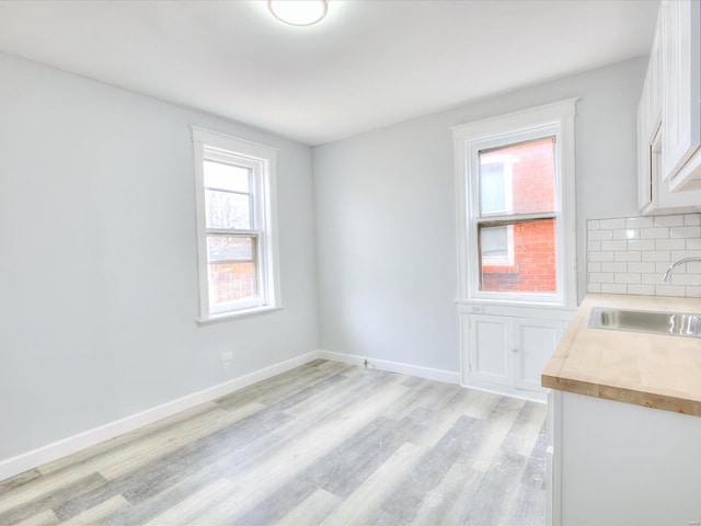 unfurnished dining area featuring a sink, baseboards, and light wood-style flooring