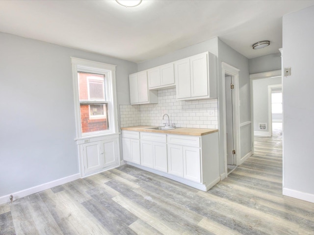 kitchen featuring tasteful backsplash, butcher block countertops, light wood-style floors, and a sink