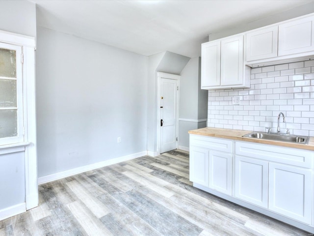 kitchen with tasteful backsplash, baseboards, butcher block countertops, light wood-style floors, and a sink