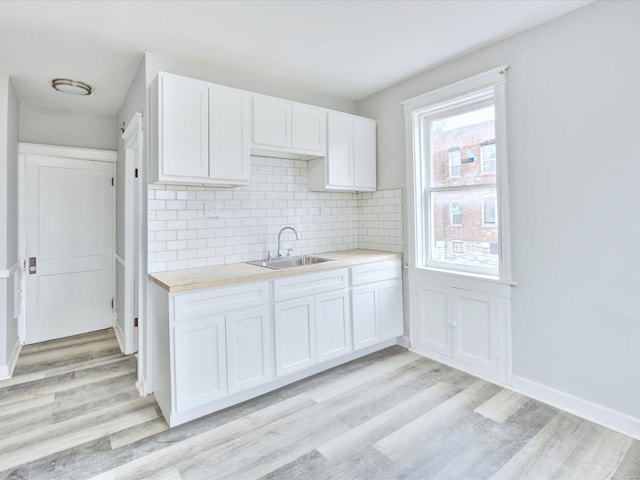 kitchen with a sink, tasteful backsplash, light wood-style floors, white cabinets, and light countertops