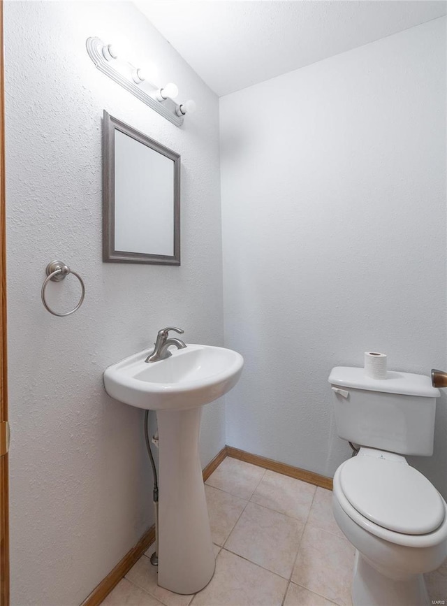 half bathroom with tile patterned floors, toilet, and baseboards