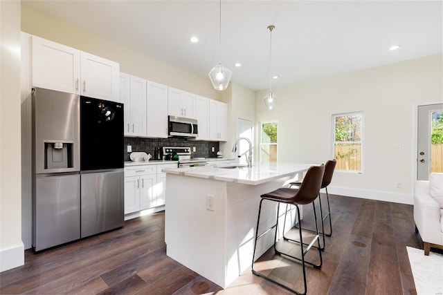 kitchen with a center island with sink, a sink, tasteful backsplash, white cabinetry, and stainless steel appliances