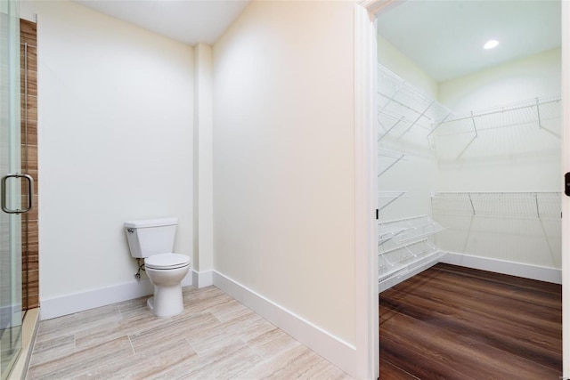 bathroom with toilet, wood finished floors, and a spacious closet