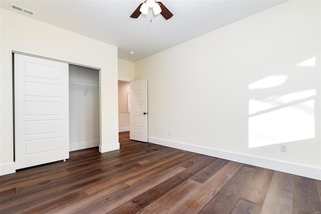 unfurnished bedroom featuring dark wood-style floors, visible vents, baseboards, ceiling fan, and a closet