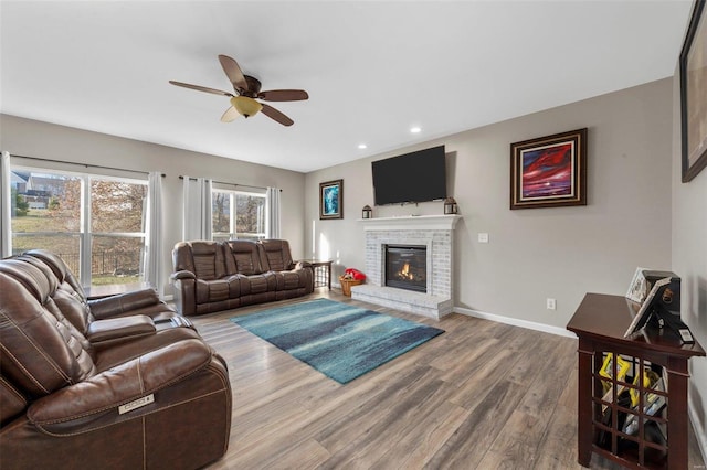 living area with a ceiling fan, wood finished floors, recessed lighting, baseboards, and a brick fireplace