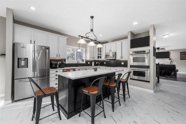 kitchen with a breakfast bar area, stainless steel appliances, white cabinetry, marble finish floor, and backsplash