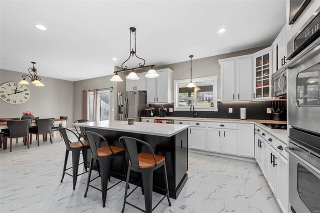 kitchen with tasteful backsplash, a kitchen island, light countertops, appliances with stainless steel finishes, and marble finish floor