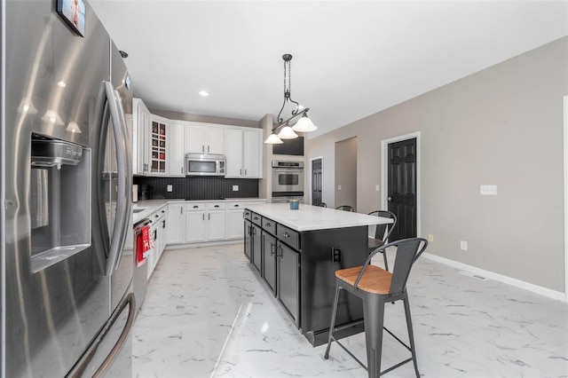 kitchen with marble finish floor, a kitchen breakfast bar, white cabinetry, appliances with stainless steel finishes, and baseboards