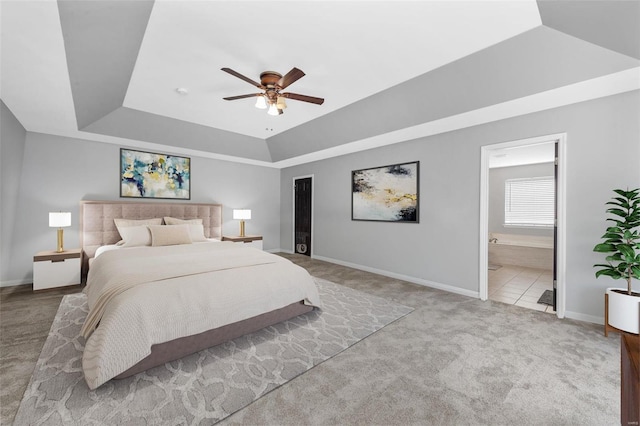 carpeted bedroom with baseboards, ensuite bathroom, a tray ceiling, and a ceiling fan