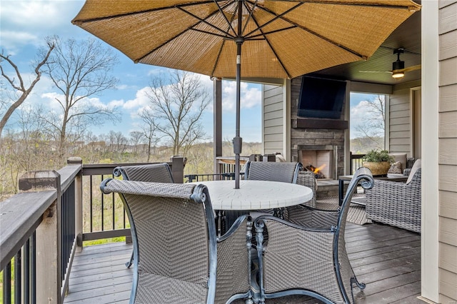 wooden deck featuring ceiling fan, outdoor dining area, and an outdoor stone fireplace