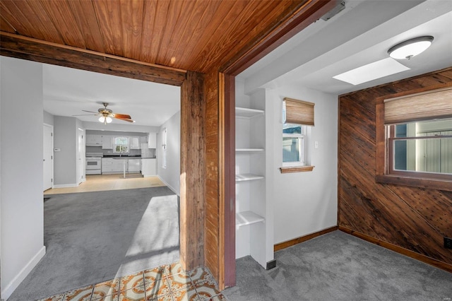 hall with light carpet, wooden walls, wood ceiling, and a skylight