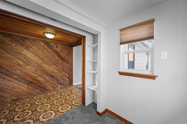 corridor featuring wood walls, baseboards, and carpet