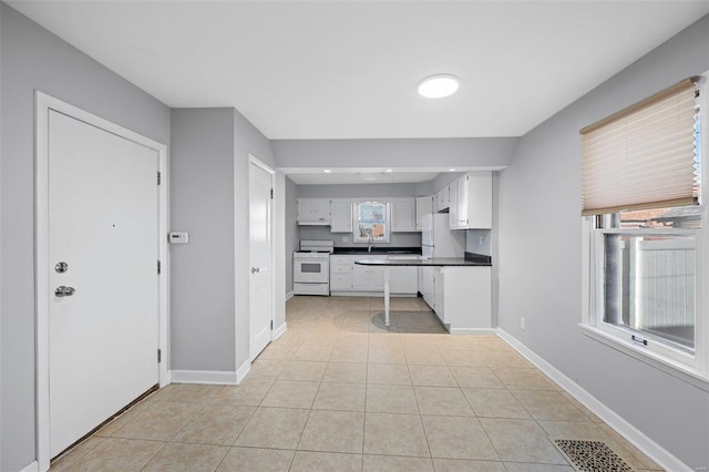 kitchen with dark countertops, baseboards, light tile patterned floors, white cabinets, and white appliances