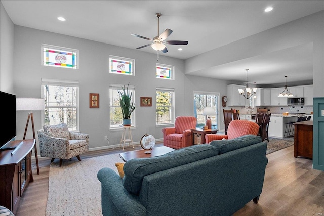 living area with recessed lighting, ceiling fan with notable chandelier, baseboards, and wood finished floors