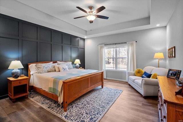 bedroom featuring a ceiling fan, wood finished floors, recessed lighting, a decorative wall, and a raised ceiling