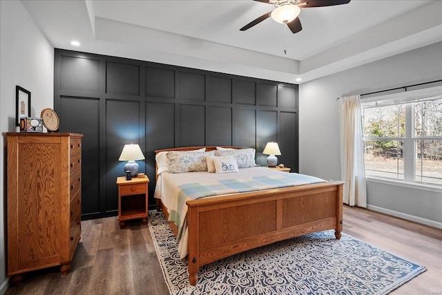 bedroom featuring a decorative wall, baseboards, a ceiling fan, and wood finished floors