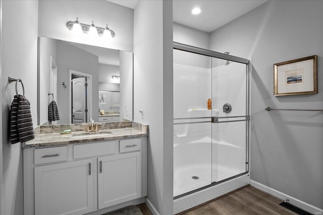 full bath with baseboards, vanity, wood finished floors, and a shower stall