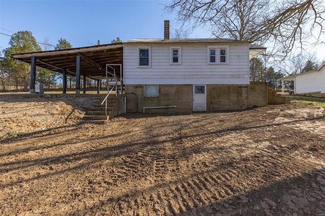 back of property featuring an outdoor structure, a carport, and a chimney