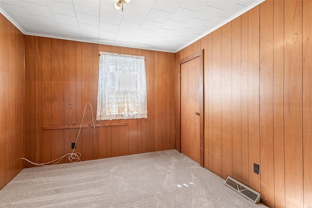 carpeted empty room featuring visible vents and wooden walls