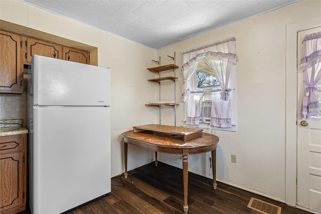 kitchen with brown cabinetry, visible vents, freestanding refrigerator, and dark wood-style floors