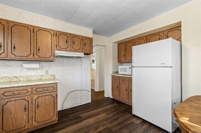 kitchen featuring white appliances, dark wood finished floors, light countertops, under cabinet range hood, and brown cabinets