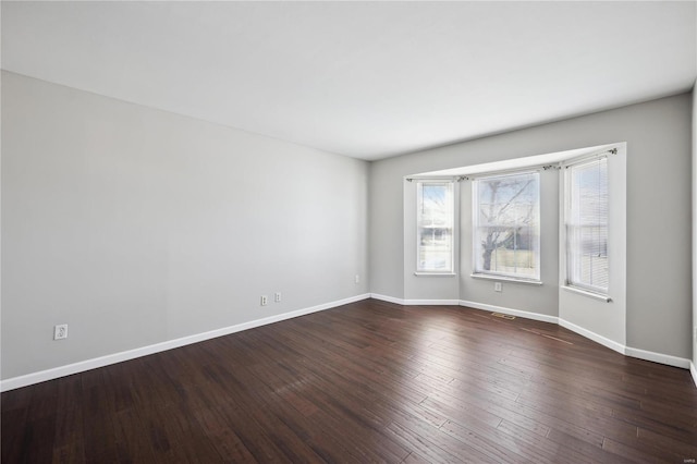 empty room with dark wood-type flooring, visible vents, and baseboards