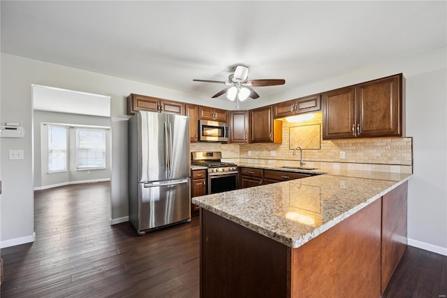 kitchen featuring a sink, light stone counters, backsplash, stainless steel appliances, and a peninsula