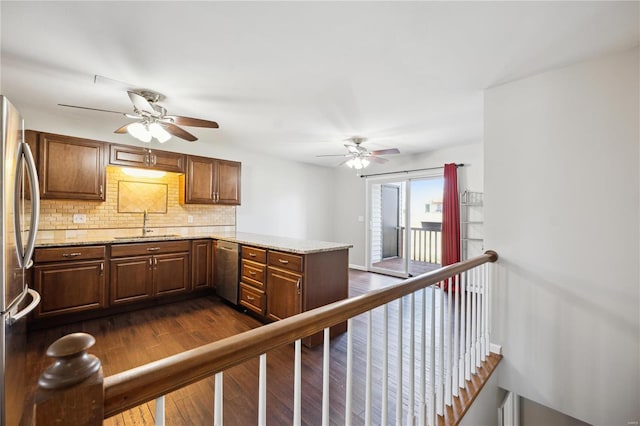 kitchen featuring tasteful backsplash, dark wood finished floors, a peninsula, stainless steel appliances, and a sink