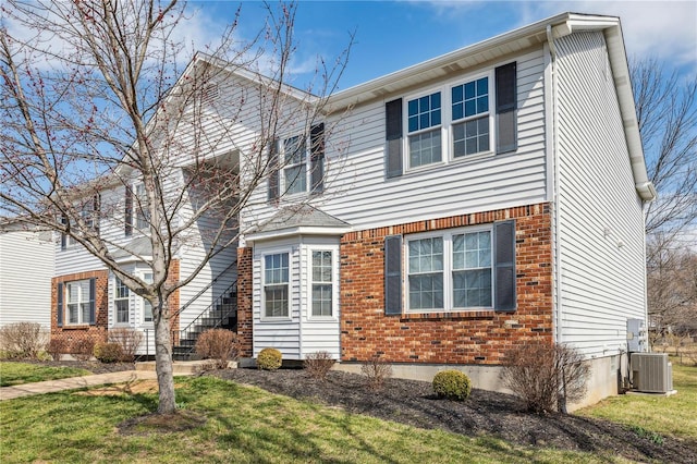 traditional-style home with brick siding, a front yard, and central AC