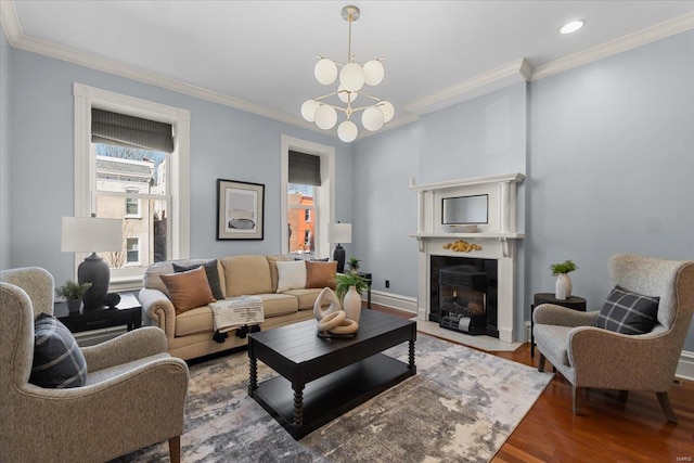 living area with a fireplace with flush hearth, ornamental molding, wood finished floors, baseboards, and a chandelier