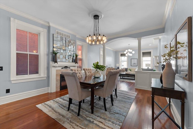 dining space featuring ornate columns, arched walkways, dark wood-style flooring, crown molding, and a chandelier