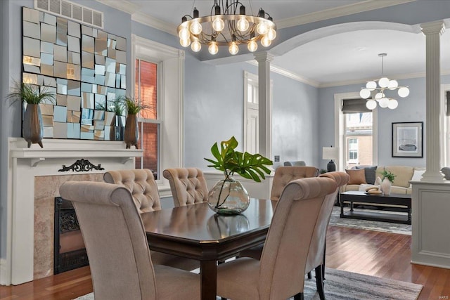 dining area featuring wood finished floors, decorative columns, arched walkways, crown molding, and a chandelier