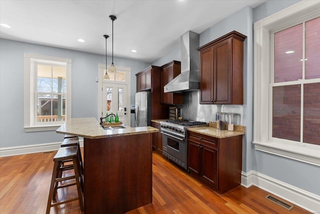 kitchen featuring visible vents, dark wood finished floors, a sink, stainless steel appliances, and wall chimney range hood