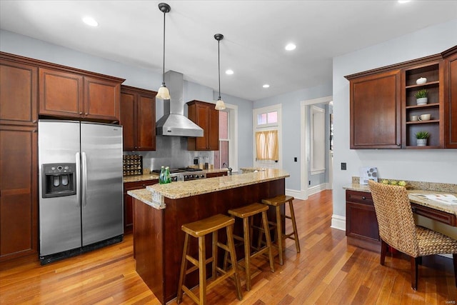 kitchen with a kitchen bar, wall chimney range hood, stainless steel refrigerator with ice dispenser, and light wood-type flooring