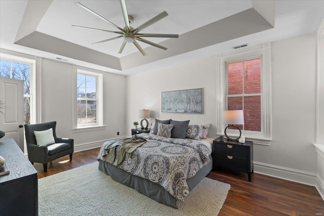 bedroom featuring a tray ceiling, baseboards, visible vents, and wood finished floors