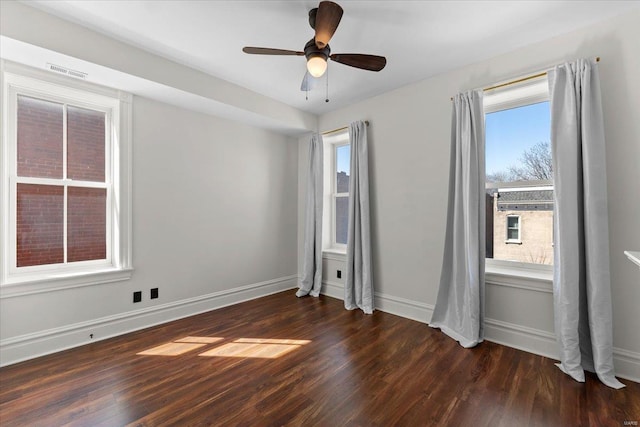 spare room featuring visible vents, a ceiling fan, baseboards, and dark wood-style flooring