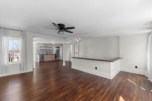 unfurnished living room featuring dark wood finished floors, bar, beverage cooler, and visible vents