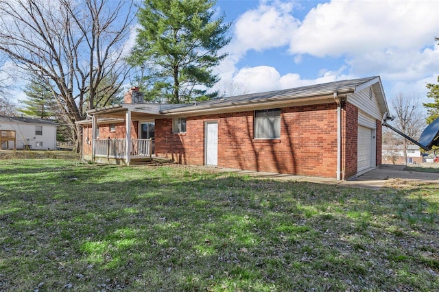 rear view of house with brick siding, an attached garage, a chimney, and a yard